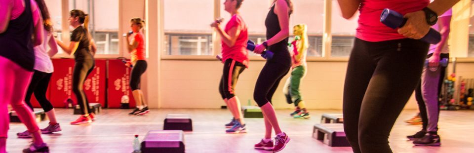 Lezione di fitness al chiuso con persone che usano pesi e step