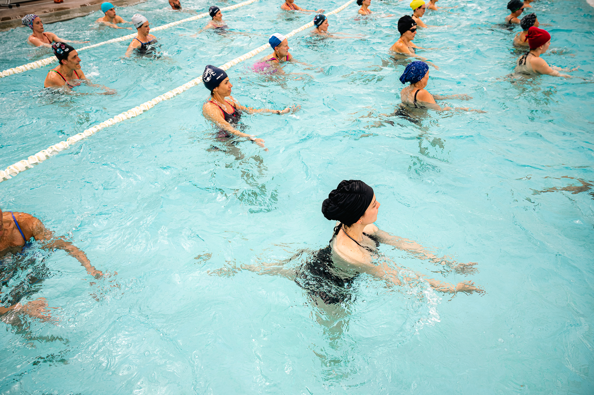 Gruppo di persone che partecipa a una lezione di ginnastica in acqua, eseguendo esercizi in piscina.
