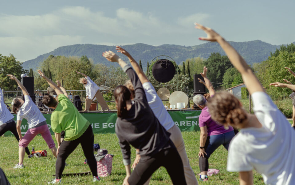 Partecipanti che eseguono esercizi di stretching guidati da un istruttore su un palco all'aperto.